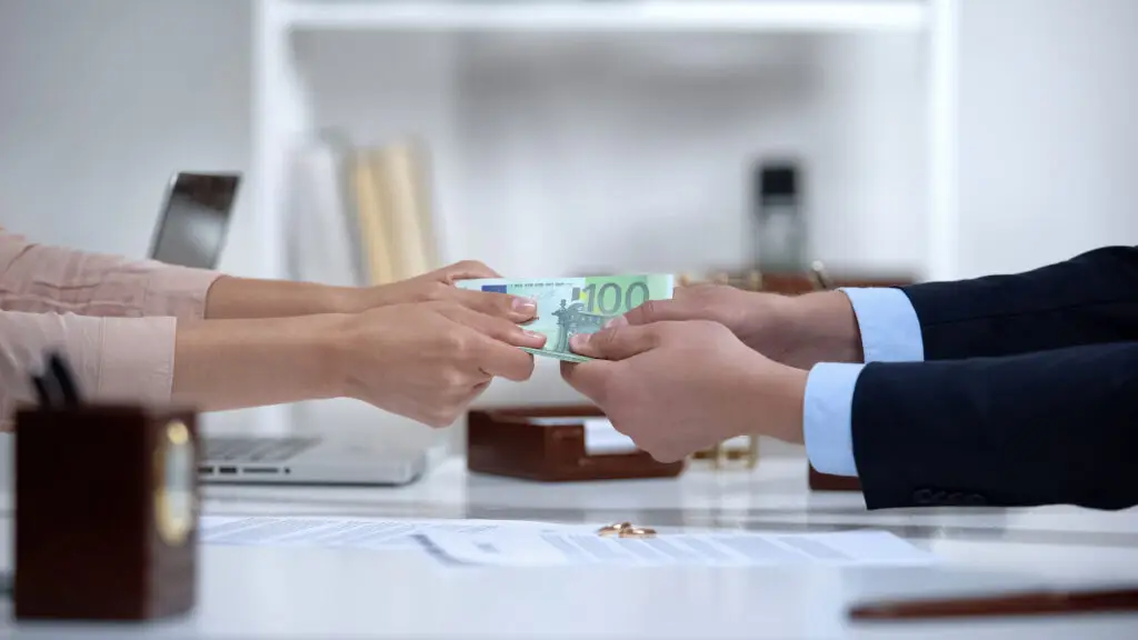 Two pairs of hands exchanging a $100 bill.